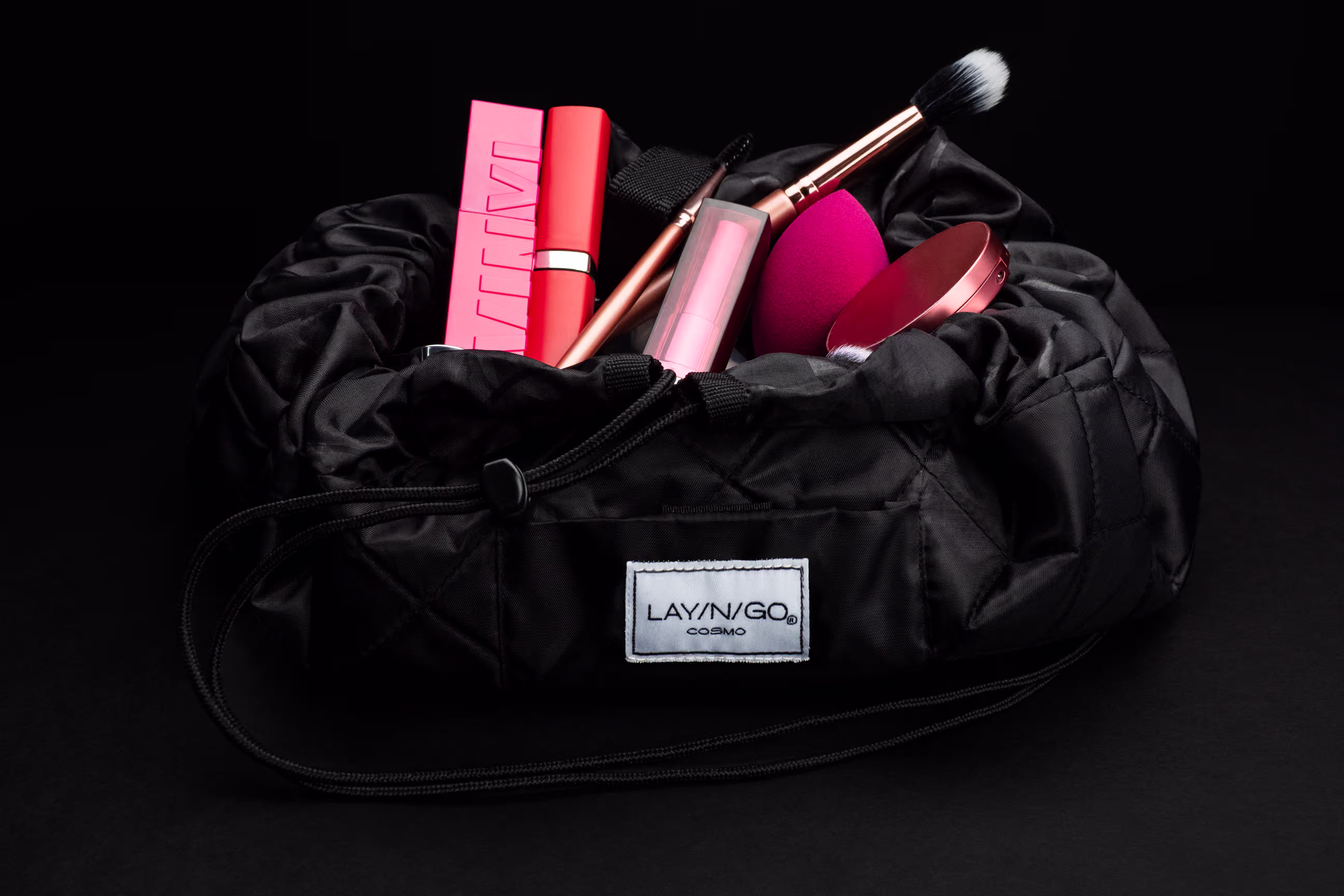Lay-N-Go Cosmo makeup bag opened with cosmetics and brushes displayed inside on a black background in a styled product photograph