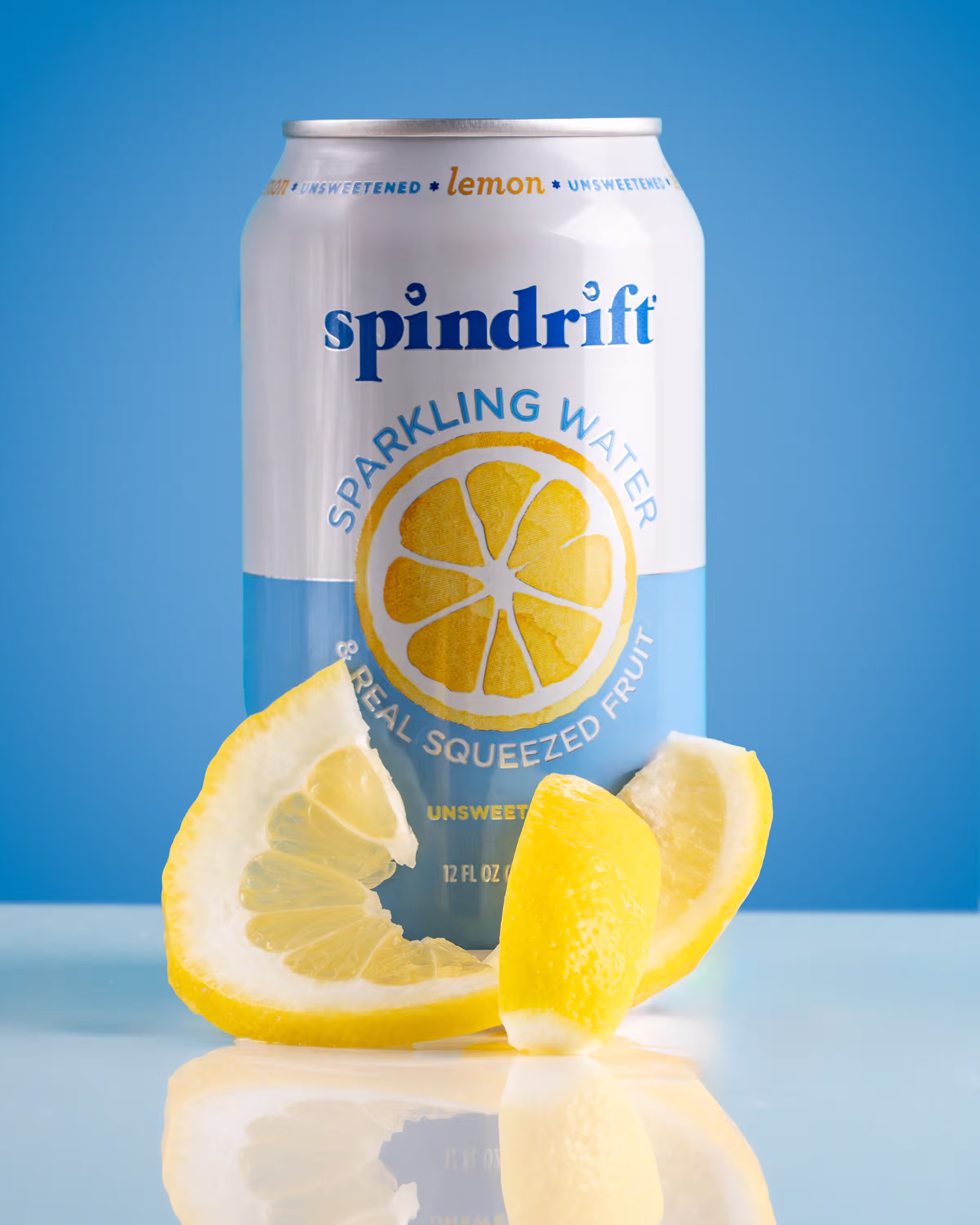 Spindrift lemon sparkling water can with fresh lemon wedges on a reflective blue surface photographed with negative space for multiple crop formats