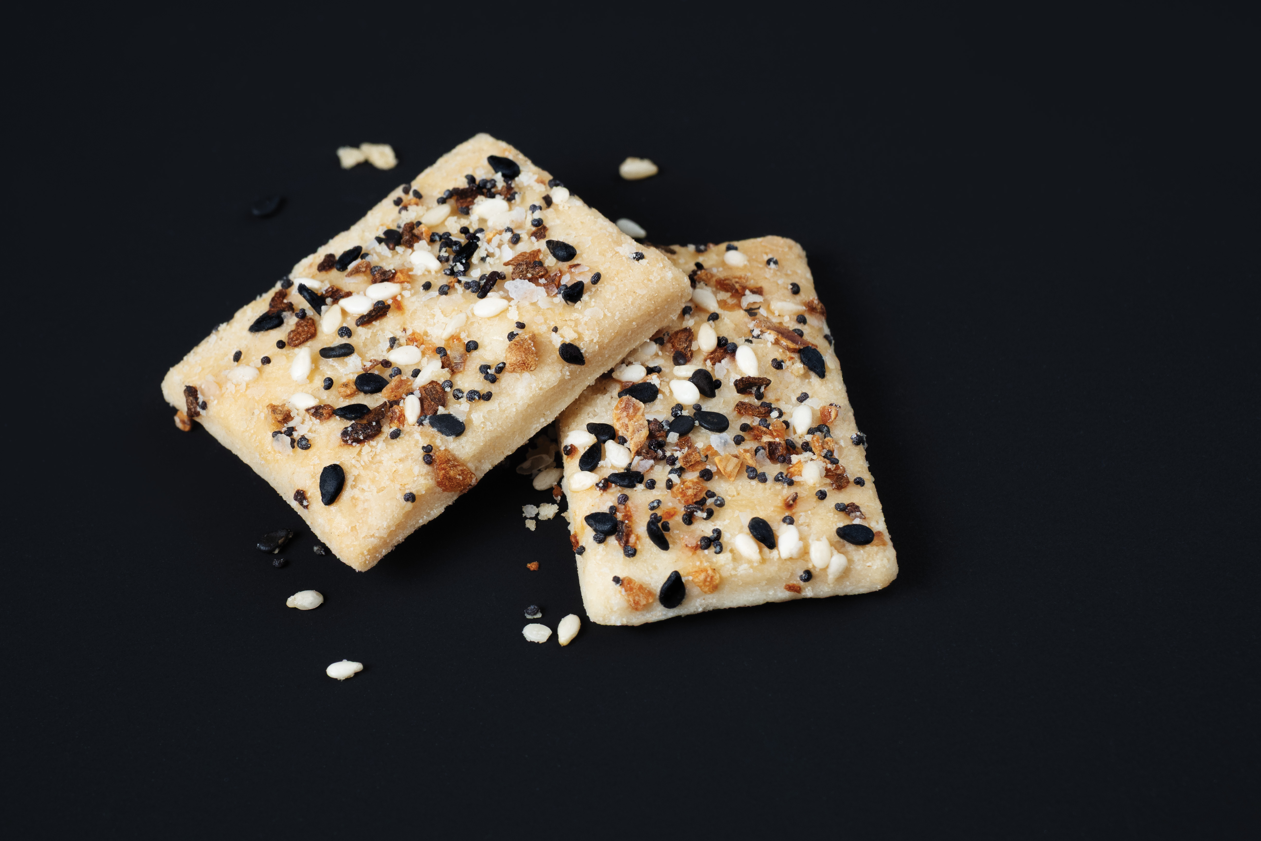 Two Great Lakes Pot Pies Everything Pie Chips stacked on a black background with sesame seeds and crumbs around them.