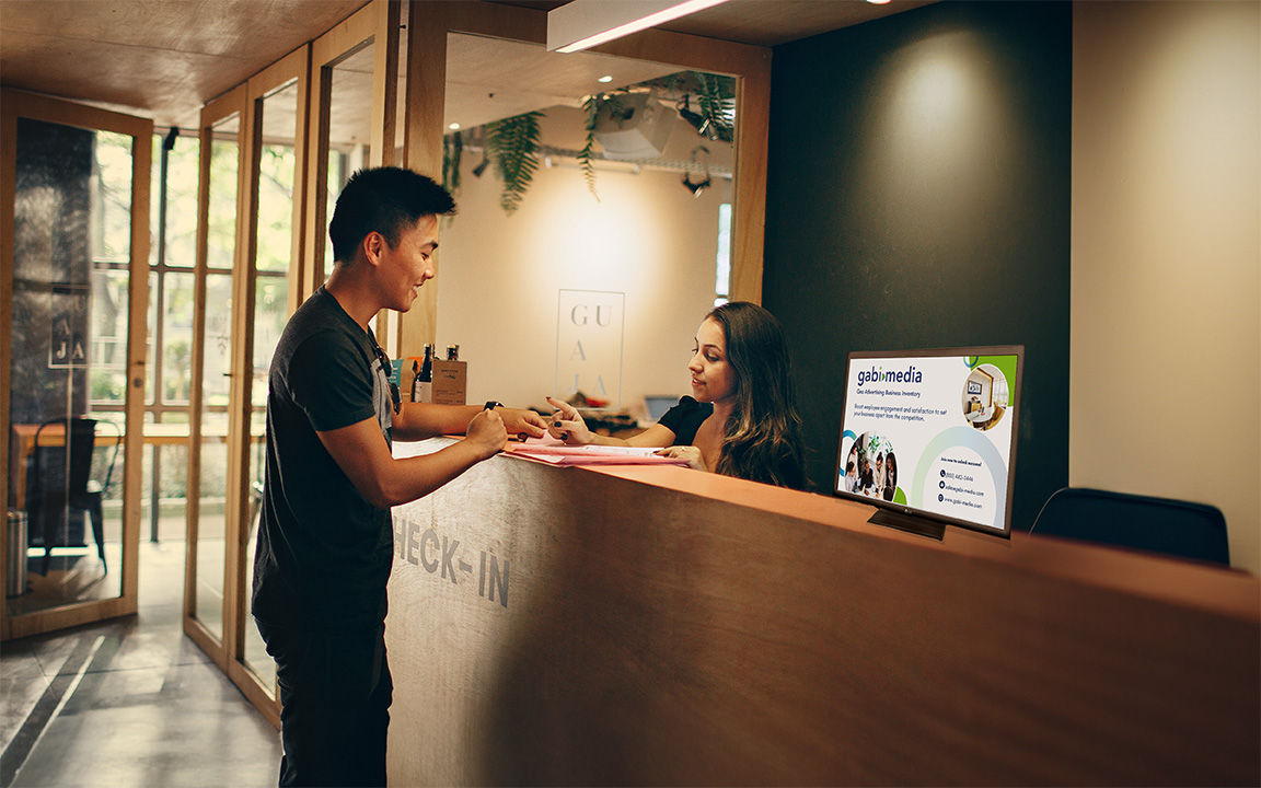A man checking into a hotel, while one of Gabi Media's screens is prominently displayed