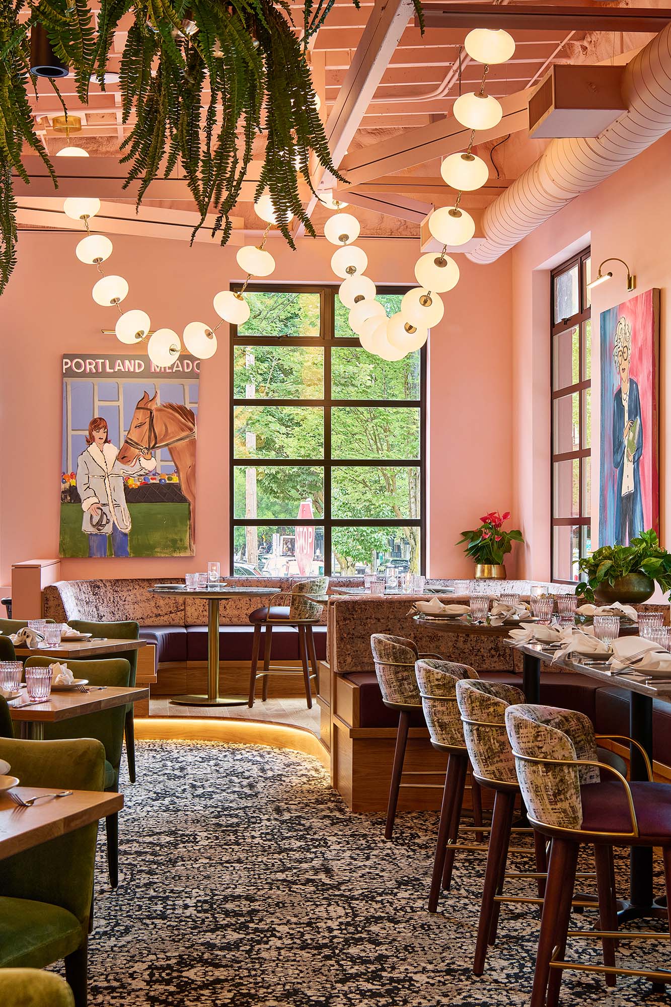 Main dining room at The Malarkey in Portland, designed by Tricorn Black, featuring pink walls, sculptural globe lighting, hanging greenery, custom banquettes and layered artwork.