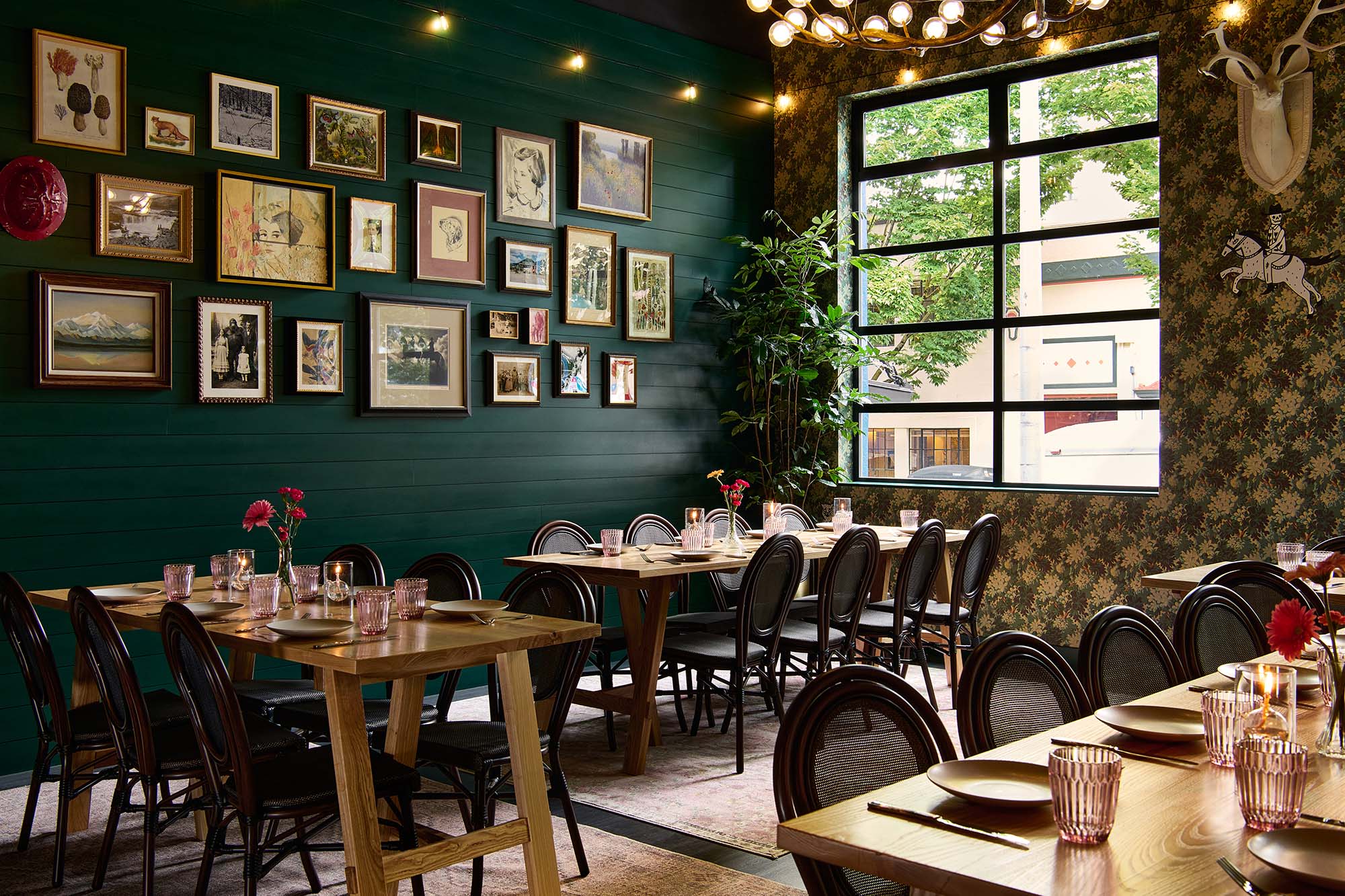 Private dining room at The Malarkey in Portland, designed by Tricorn Black, featuring a curated gallery wall, deep green paneling, patterned wallpaper and layered vintage artwork.