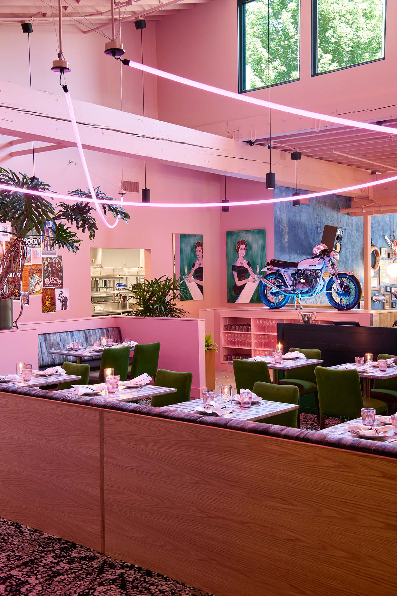 The Malarkey restaurant interior in Portland, designed by Tricorn Black, featuring pink walls, sweeping neon lighting, green dining chairs and a vintage motorcycle display.