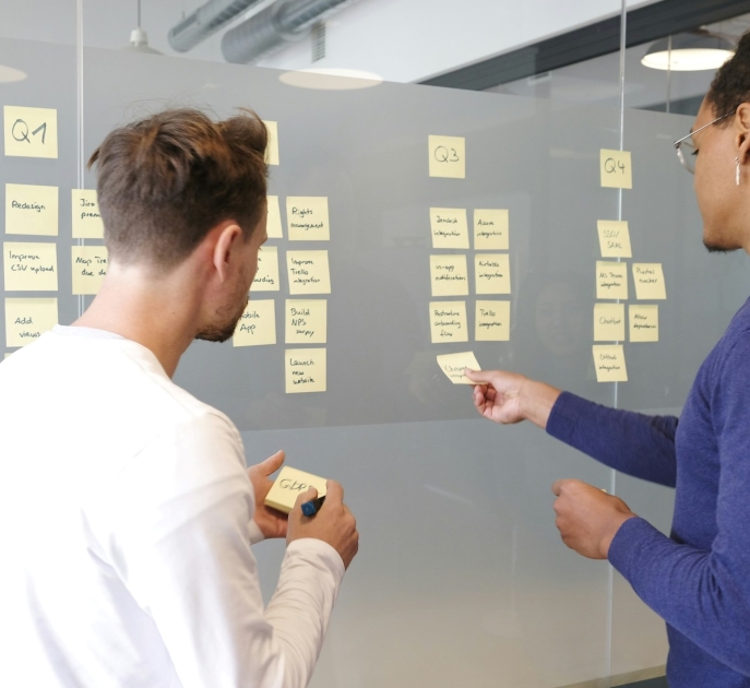 Two men organizing sticky notes on a glass wall