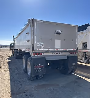 Rear view of a silver dump truck parked on a dirt surface under a clear blue sky.