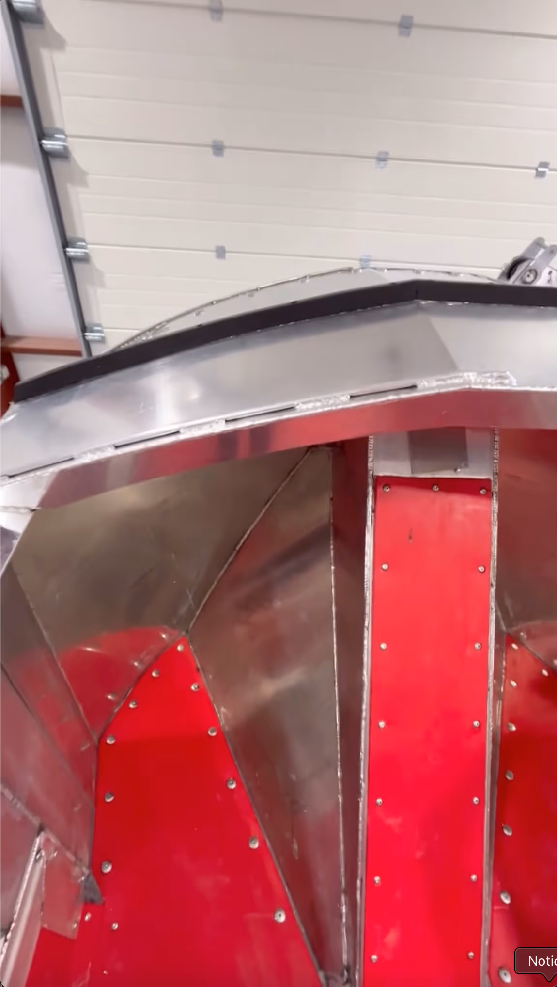 Interior section of a metallic structure with red-painted panels and rivets inside a garage with a closed white sectional door.