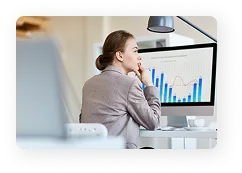 Woman sitting at a desk looking thoughtfully at a computer screen displaying various charts and graphs.