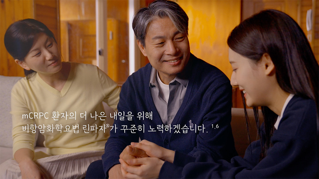 Three people sitting together indoors, smiling and holding hands in a supportive gesture.