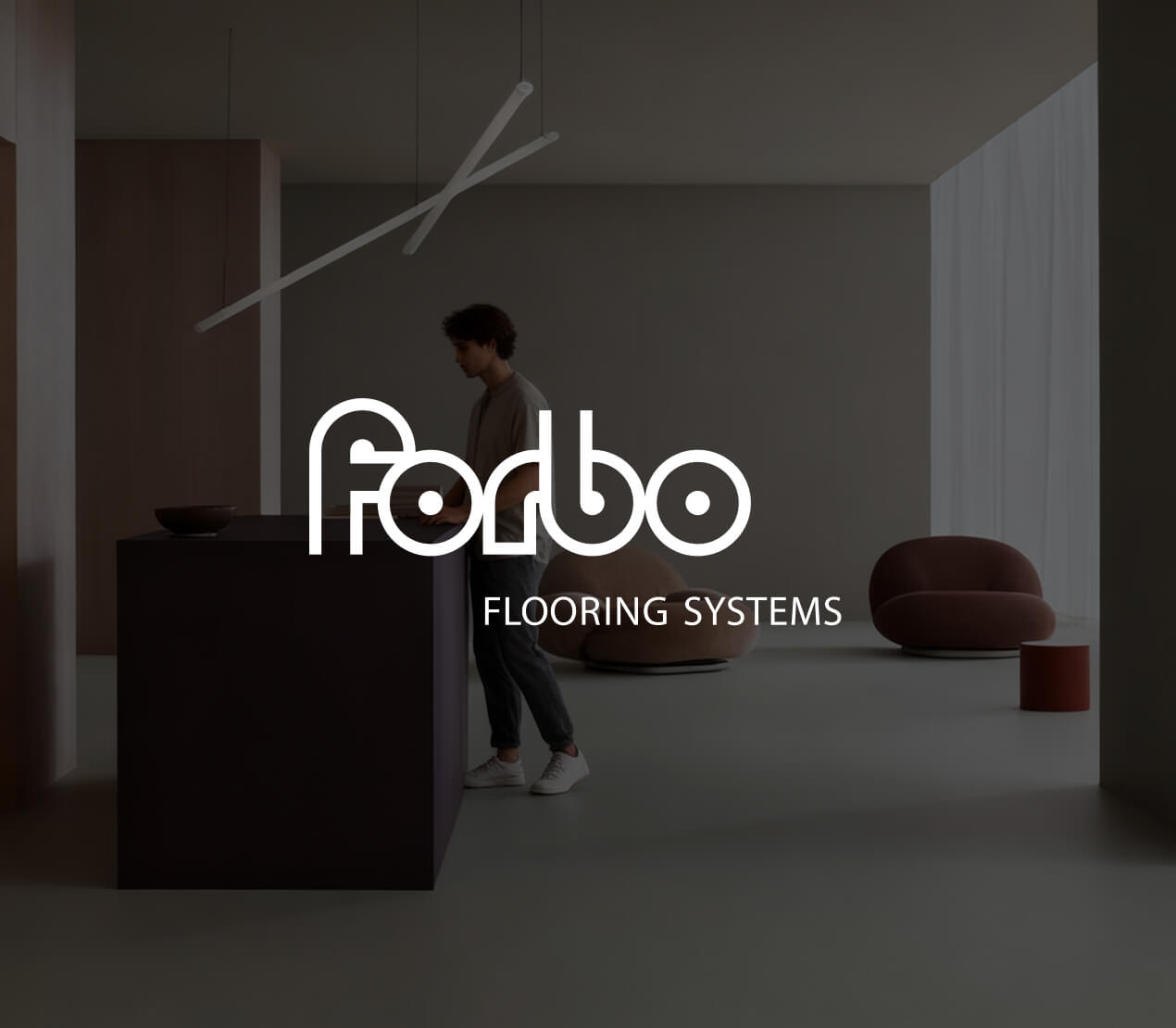 Moderner Innenraum mit einem dunkelgrauen Tresen, einem stehenden Mann, und zwei bequemen Stühlen in gedeckten Farben.