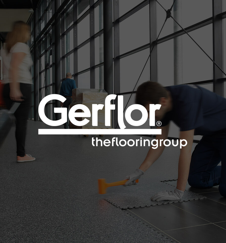 Mann kniet und verlegt Bodenbelag in einem modernen, lichtdurchfluteten Gebäude mit großen Fenstern.