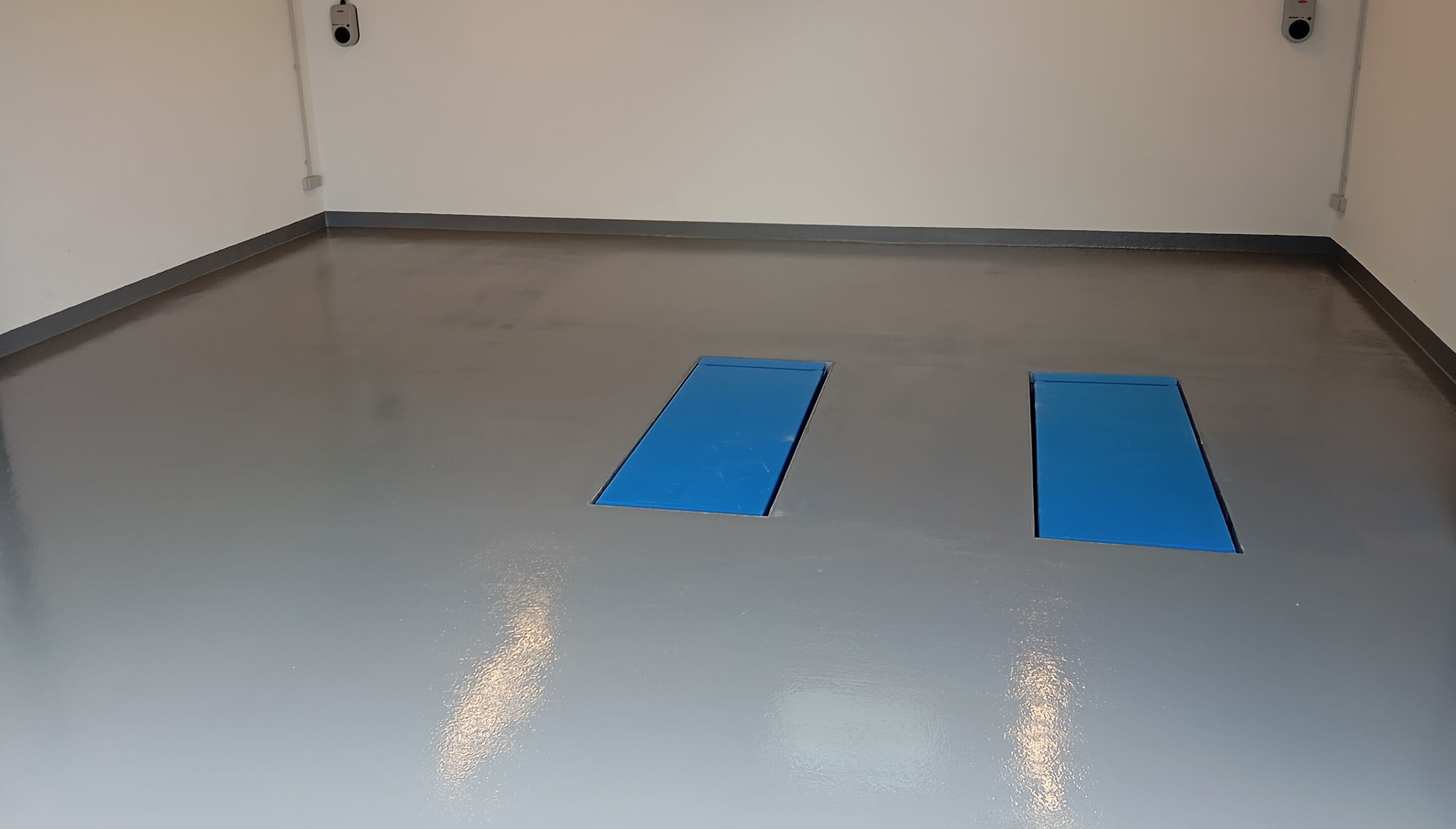 Glänzender grauer Boden in einem leeren Raum mit zwei rechteckigen blauen Abdeckungen im Boden.
