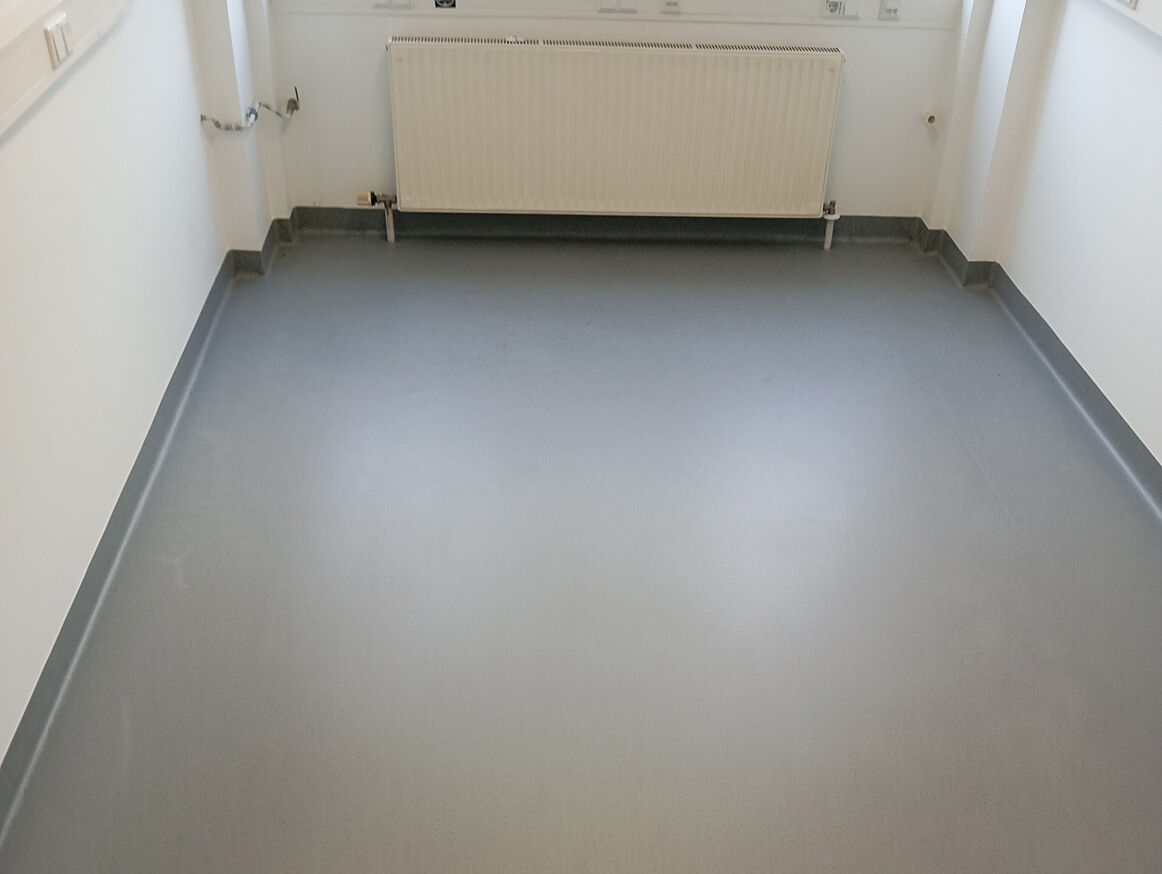 Leerer Raum mit grauem Boden und einer Wandheizung unter dem Fenster.