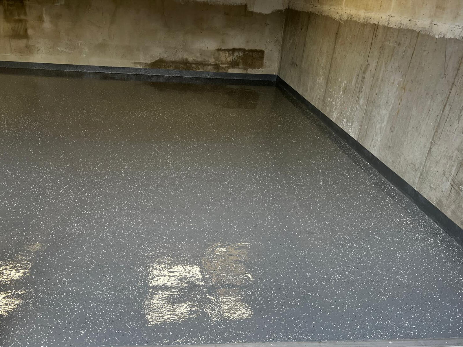 Boden mit glänzendem, grauem Epoxidharz mit weißen Sprenkeln in einer unbehandelten Betonecke.