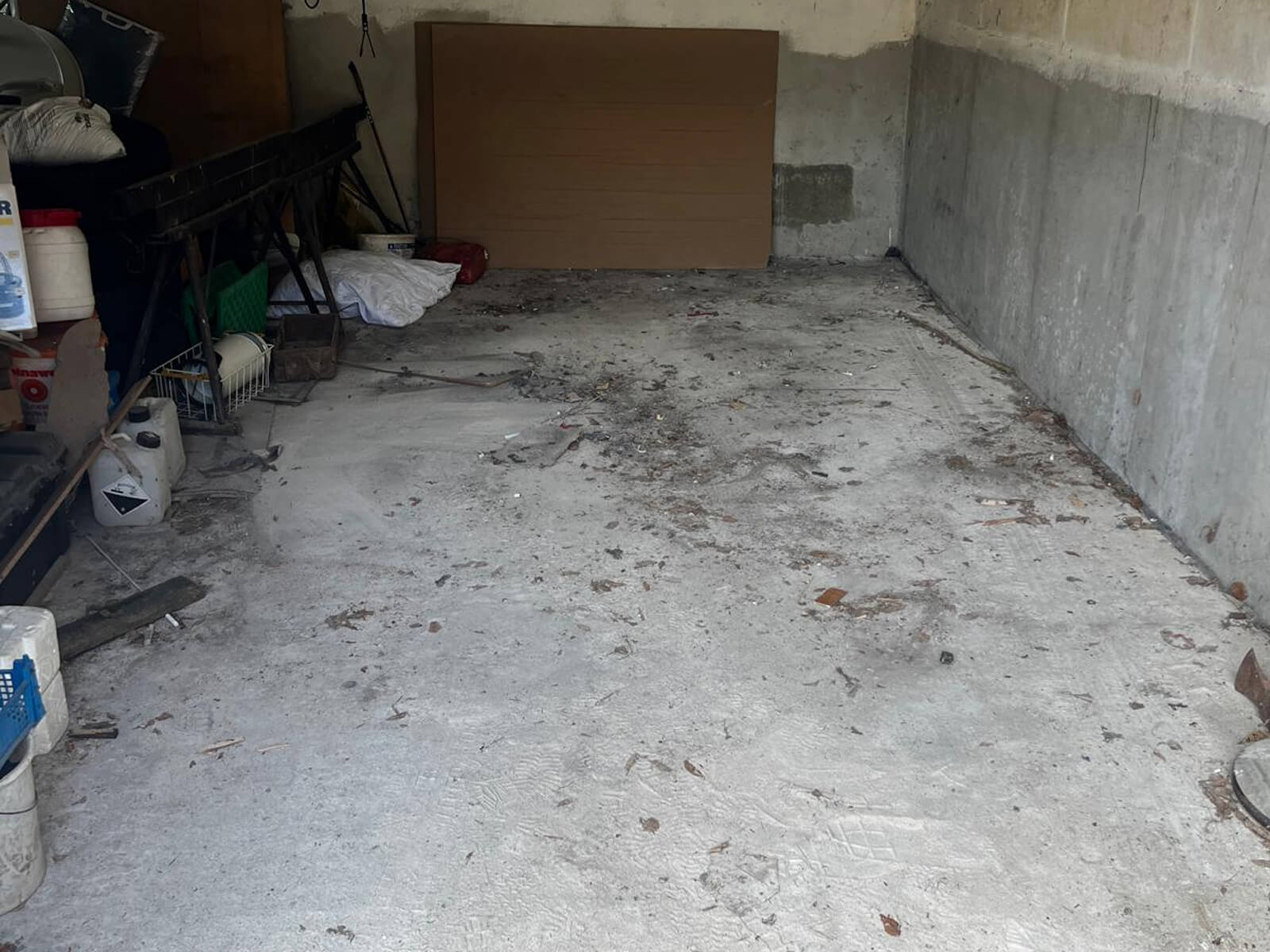 Verschmutzte Garage mit unordentlichem Boden und einigen gelagerten Gegenständen an der linken Wand.