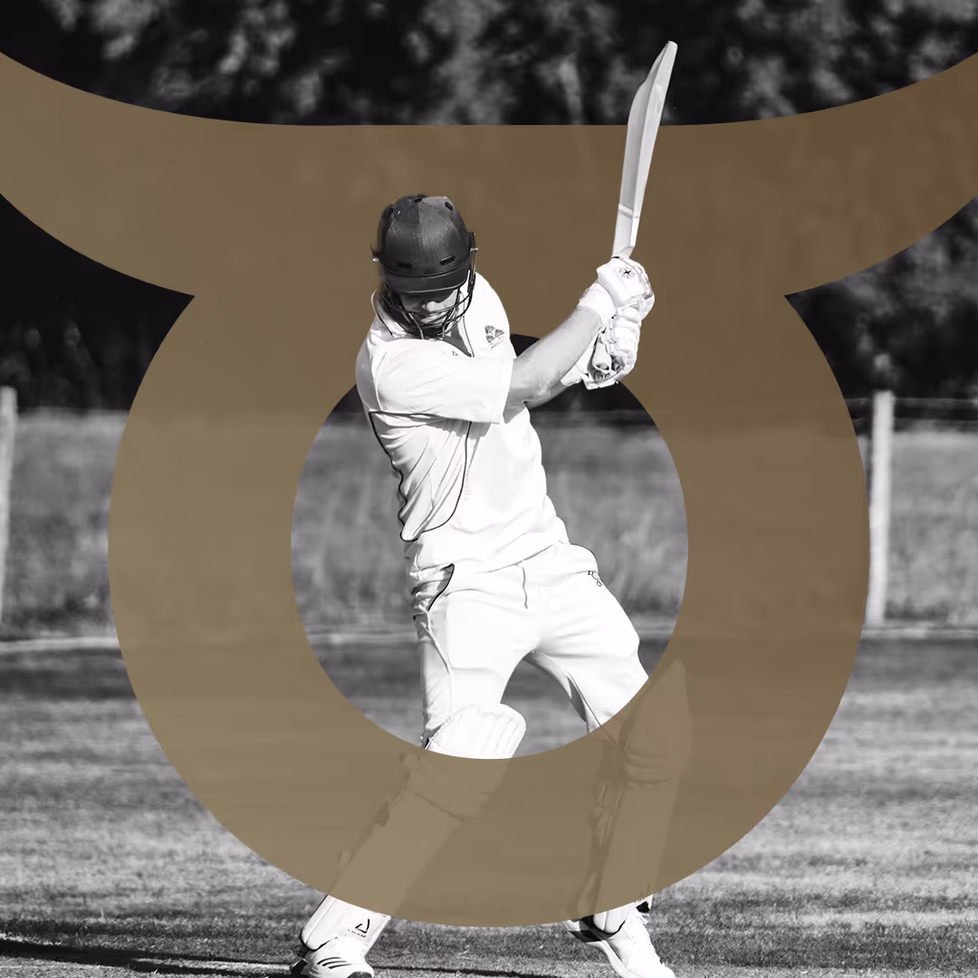 Cricket player in helmet and protective gear swinging a bat to hit the ball on a grassy field.