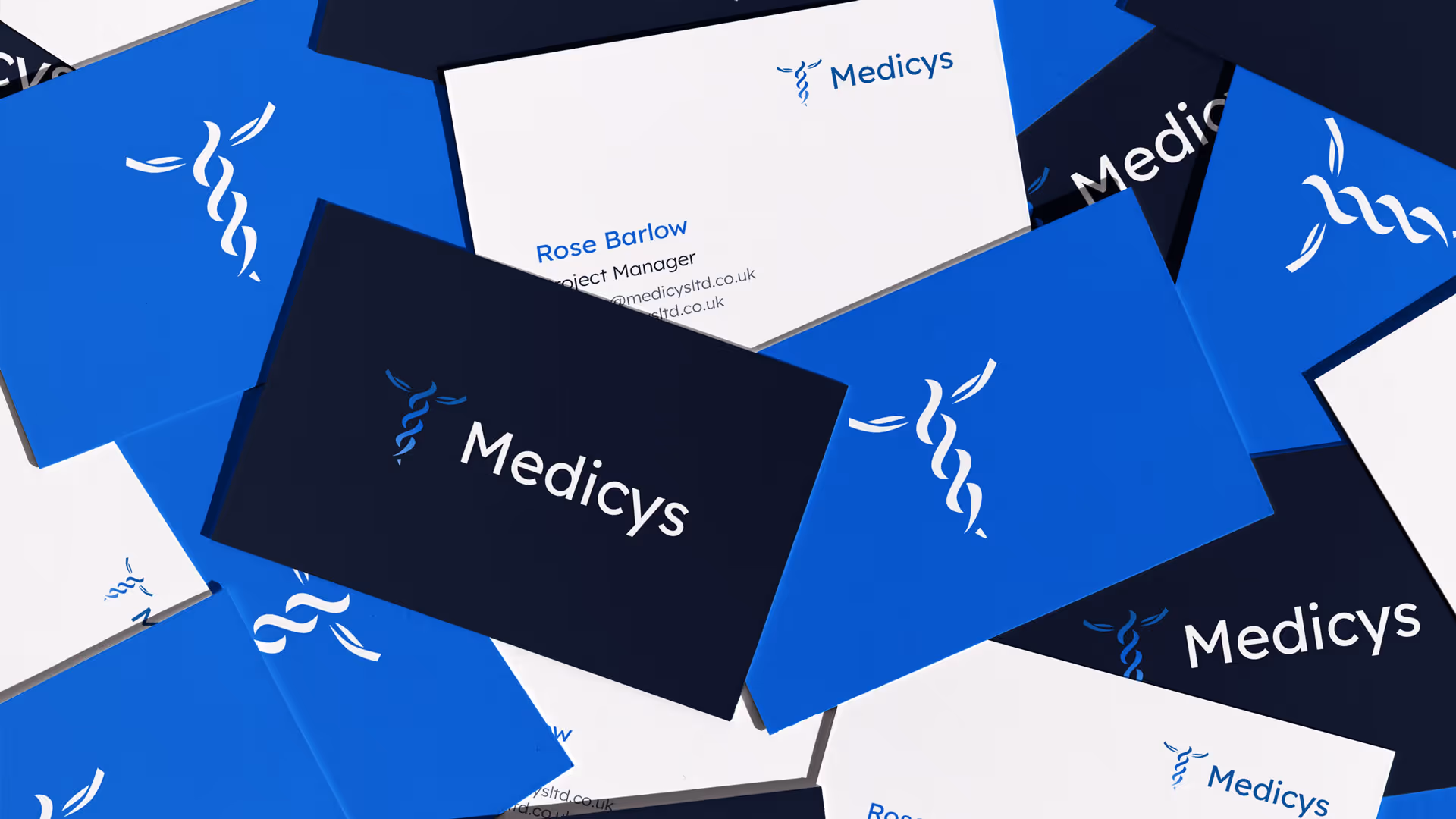 Scattered business cards for Medicys, showing a blue and white color scheme with a caduceus logo and text including Project Manager Rose Barlow.