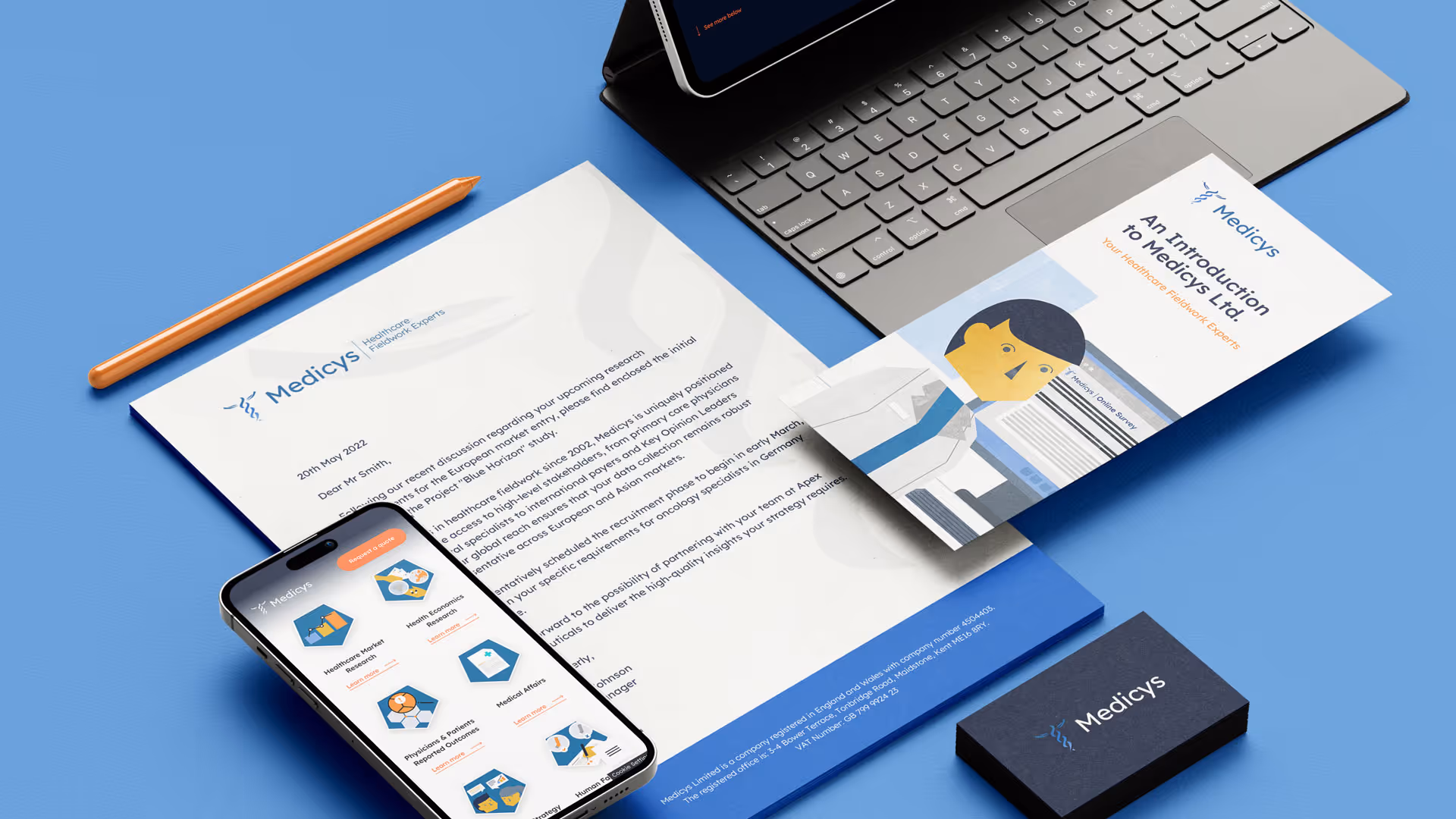 Flat lay of Medicys branded materials including a letter, a brochure with an illustrated doctor, a smartphone displaying research services, a pencil, and a business card on a blue surface.