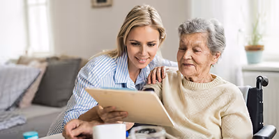 Une personne âgée et sa fille son entrain de chercher sur une tablette des informations pour embaucher une aide à domicile
