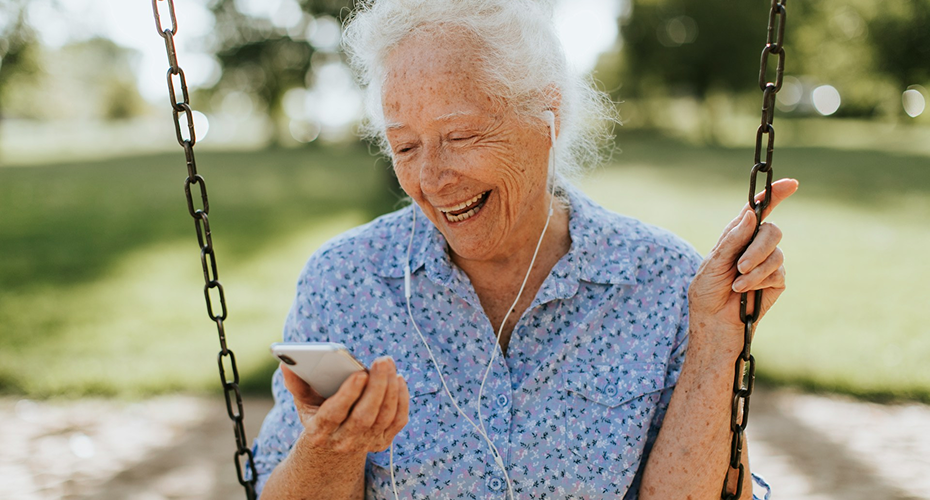 Femme senior souriante en extérieur utilisant un smartphone avec des écouteurs pour garder le lien avec ses proches.