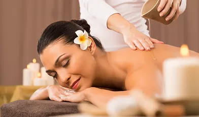 Woman with a flower in her hair receiving a relaxing back massage with oil in a spa setting.