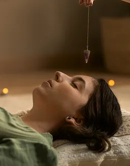 Person lying down with eyes closed, receiving a pendulum crystal healing session.