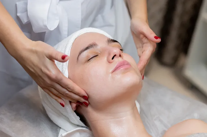 Woman receiving a facial massage with closed eyes and a towel wrapped around her head.
