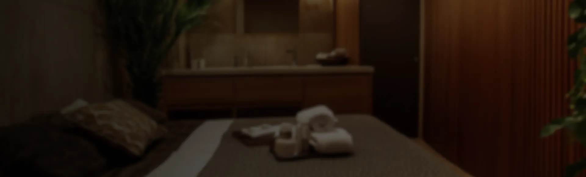 Spa treatment room with massage table covered in white towels and cozy pillows in warm ambient lighting.