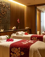 Spa room with two massage tables covered in white towels and red floral runners, decorated with pink flowers.