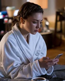 Woman in a white robe sitting indoors and looking intently at her phone.