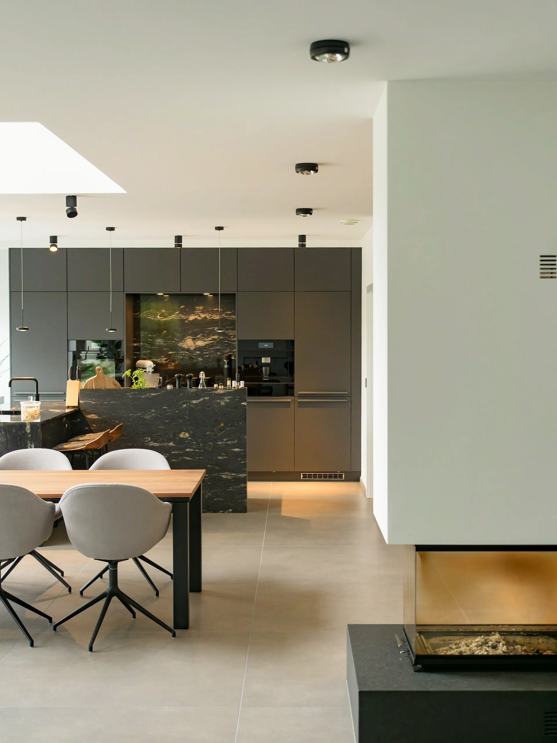 Moderne schwarze Küche mit Marmorinsel, Esstisch mit Stühlen und Kamin im Wohnraum.
