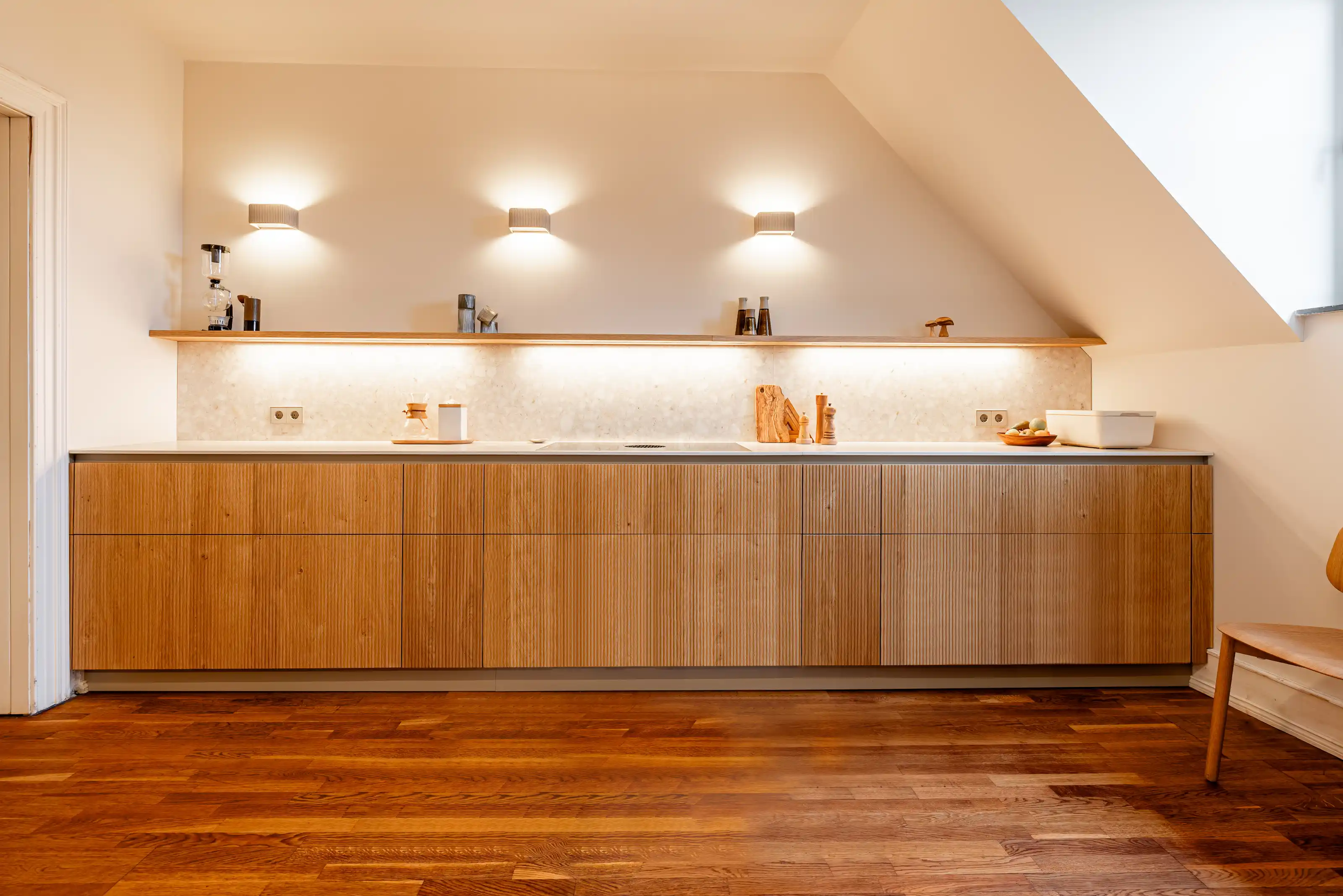 Moderne Holzküche mit Keramikarbeitsplatte, Wandregal und indirekter Beleuchtung.