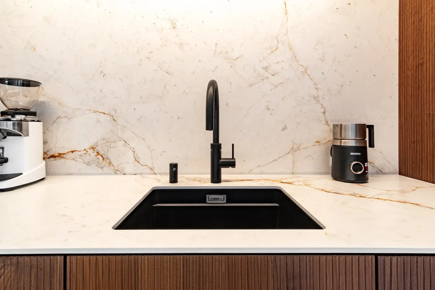 Schwarze Einbauspüle mit matt schwarzem Wasserhahn auf weißer Marmorarbeitsfläche.