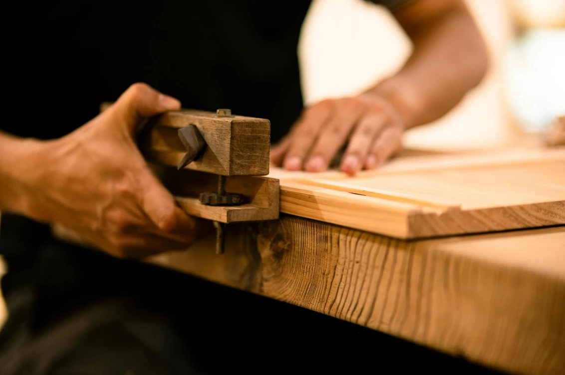 Handwerker bearbeitet Holz mit einem klassischen Zieheisen in einer Holzbearbeitungswerkstatt.