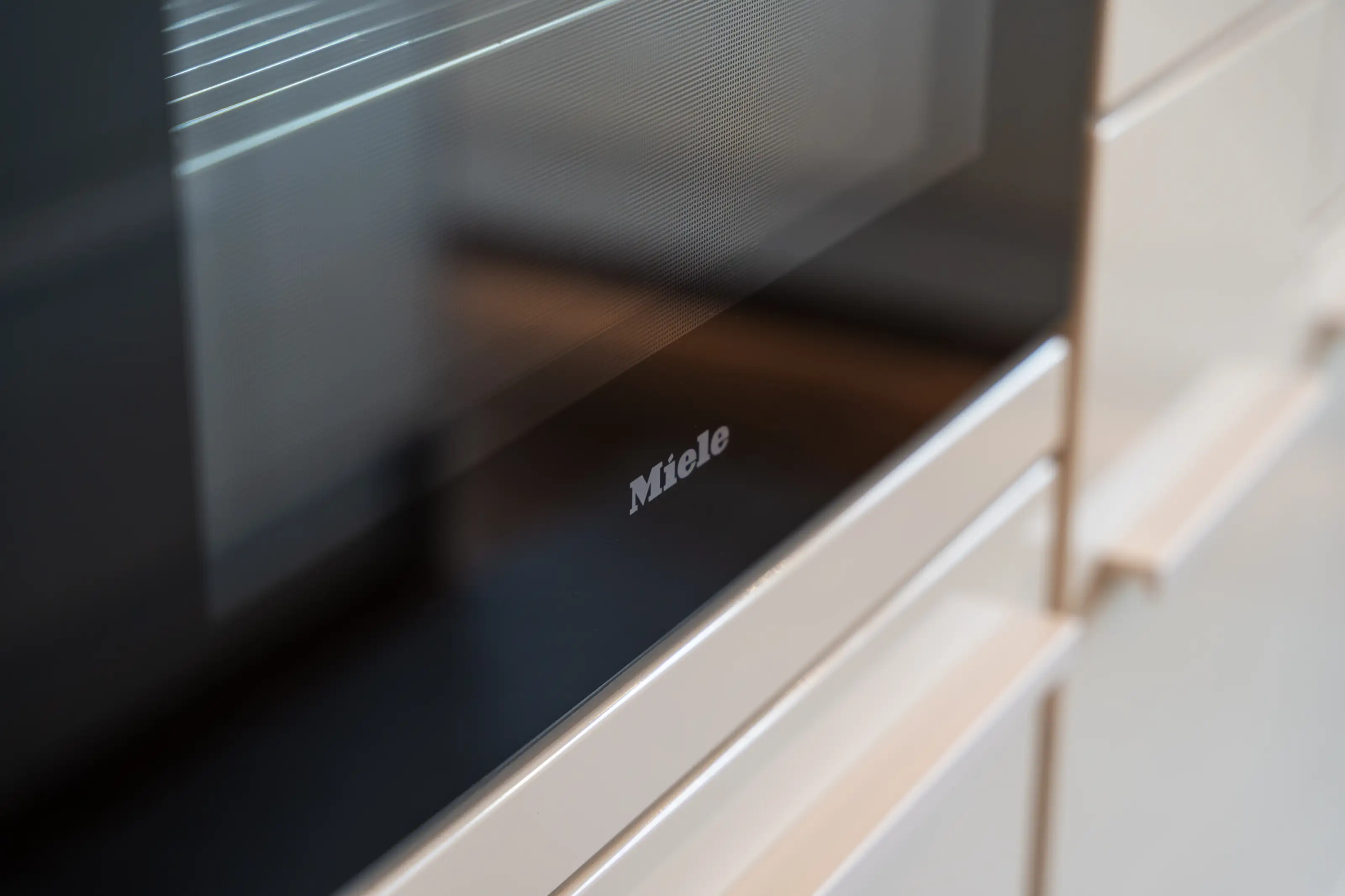 Nahaufnahme eines Miele Backofens mit schwarzer Glastür in einer hellen Küche.