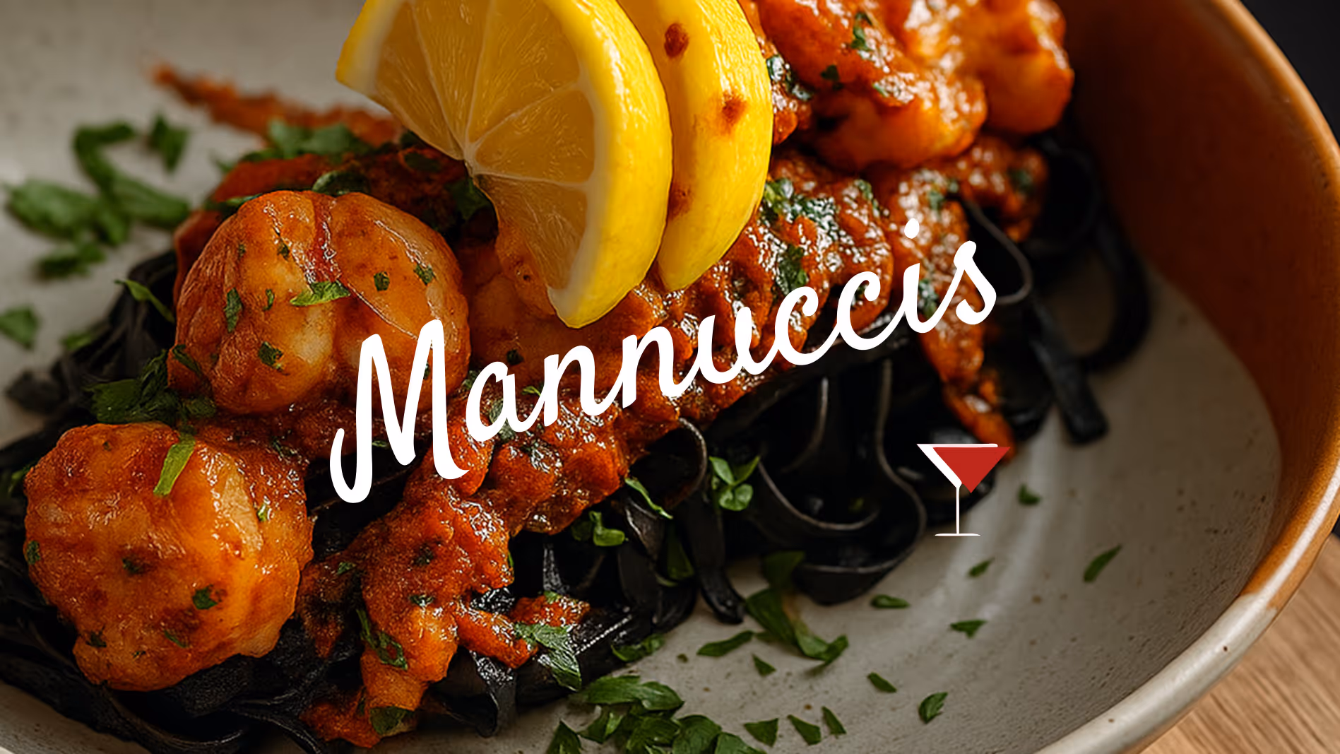 Dish of black pasta topped with shrimp in red sauce, lemon wedges, and chopped herbs.