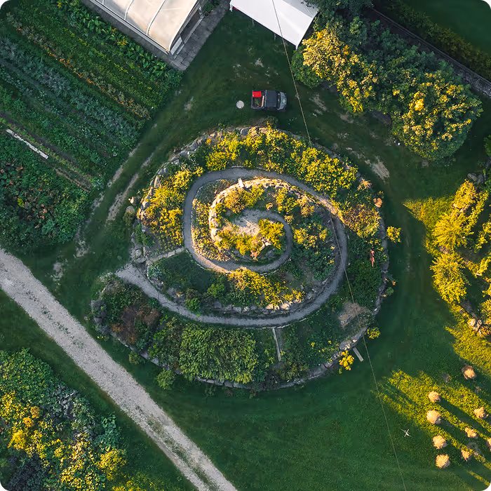 Aerial view of a spiral-shaped garden with plants and a small path around it in a green field.