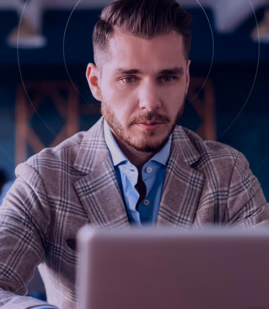 Focused man in a plaid blazer using a laptop in a modern indoor setting.