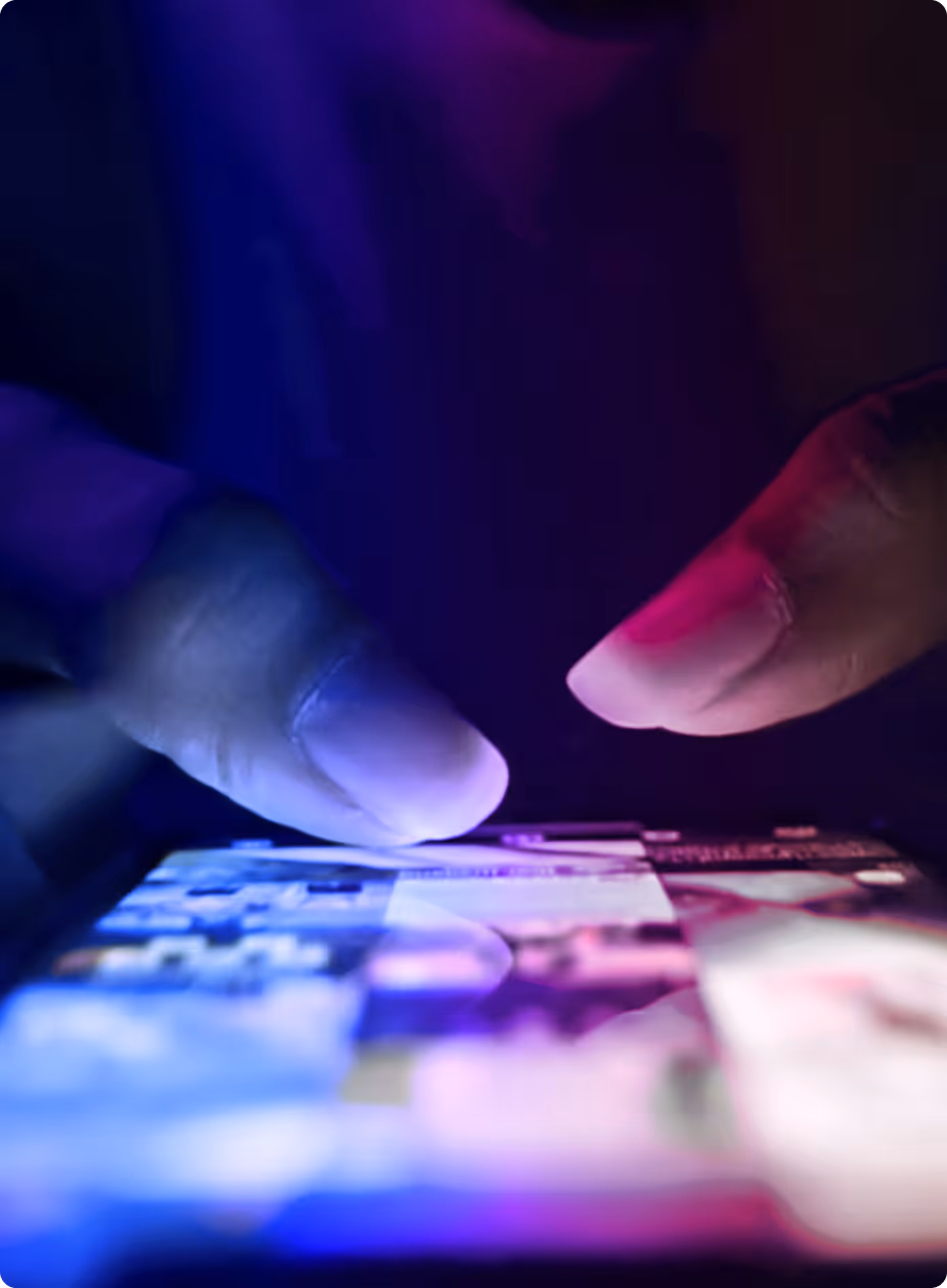 Close-up of fingers interacting with a touchscreen device under blue and purple lighting.