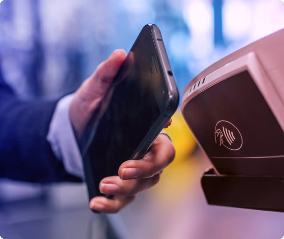 Hand holding smartphone near payment terminal for contactless mobile payment.