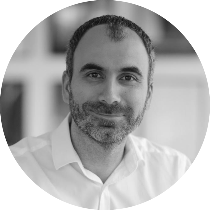 Black and white portrait of a smiling man with short hair and beard wearing a white collared shirt.