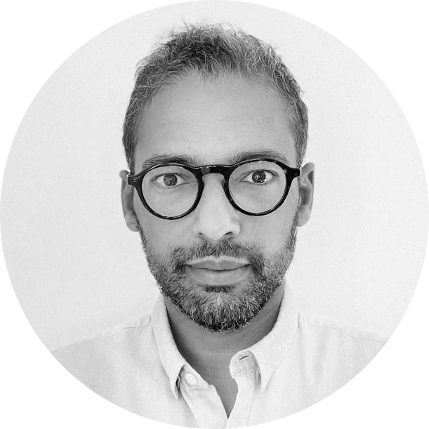 Black and white circular portrait of a man with glasses and a beard wearing a buttoned shirt.