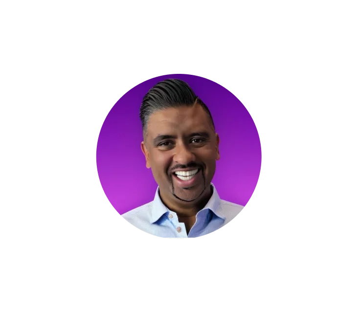 Ein lächelnder Mann mit ordentlich frisiertem schwarzem Haar und Spitzbart, der ein hellblaues Hemd mit Knöpfen trägt, vor einem violetten Hintergrund.