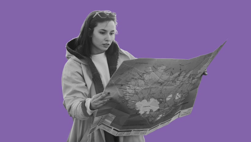Woman wearing a coat and sunglasses on her head studying a large folded map.