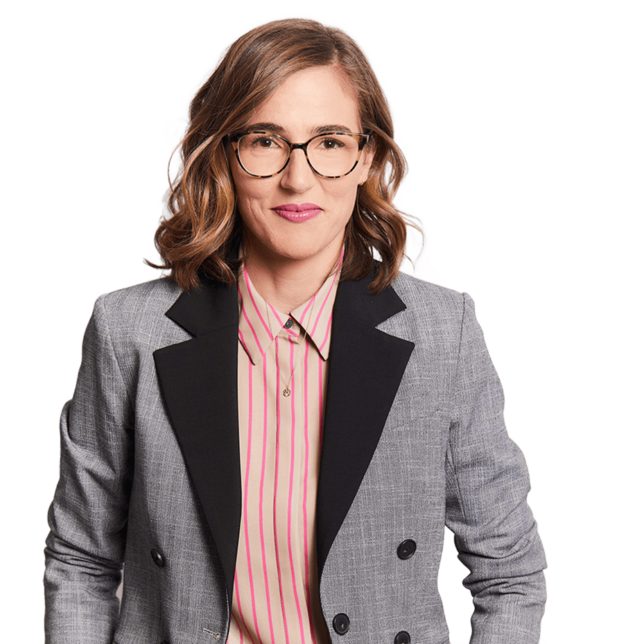 Woman with shoulder-length wavy brown hair wearing tortoiseshell glasses, a gray blazer with black lapels, and a beige shirt with pink vertical stripes.