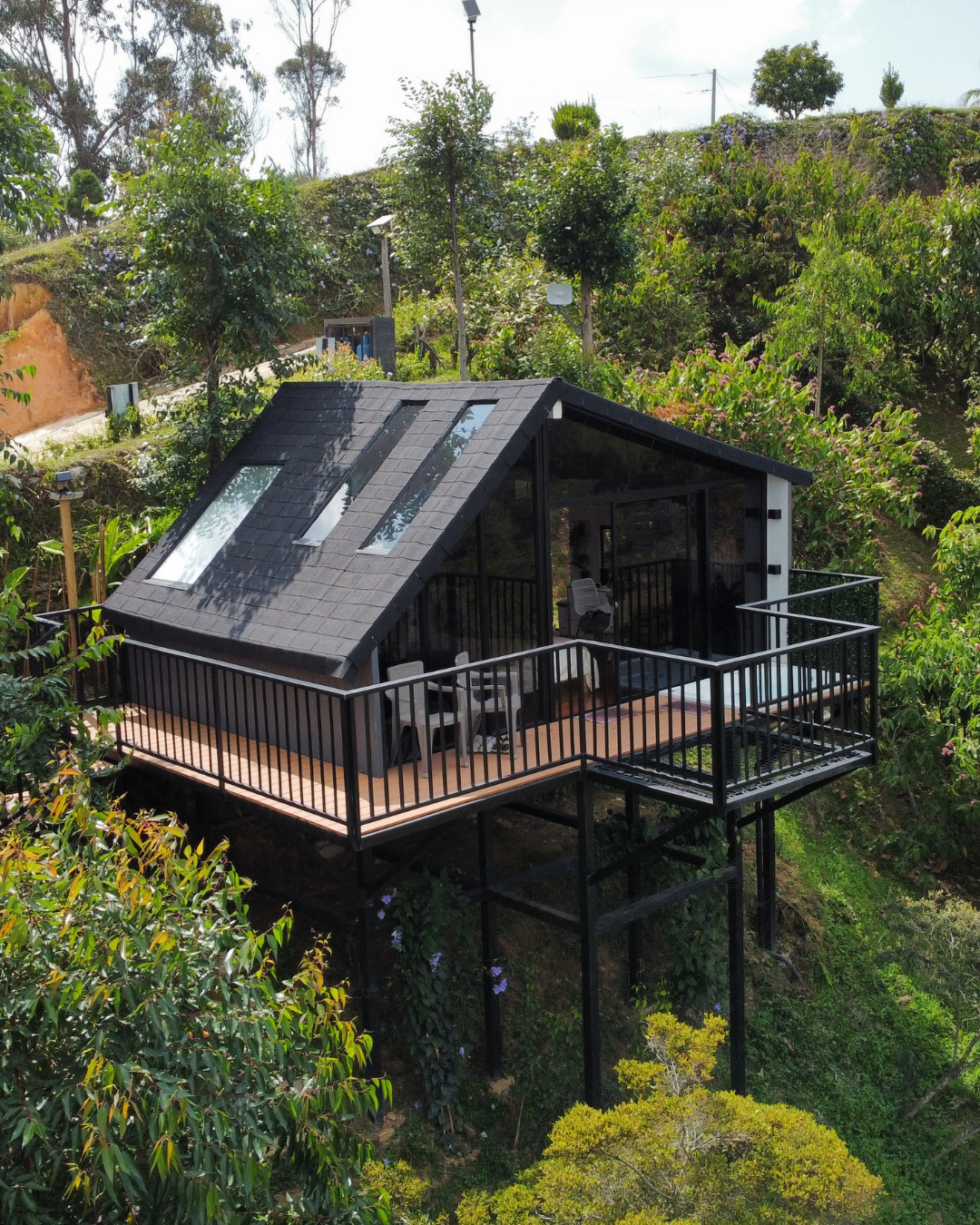Casa elevada con techo de ventanas y terraza con barandas en un entorno verde y montañoso.