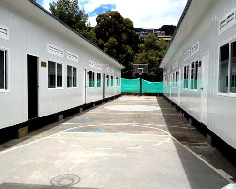 Cancha de baloncesto al aire libre entre dos edificios con paredes blancas y ventanas.