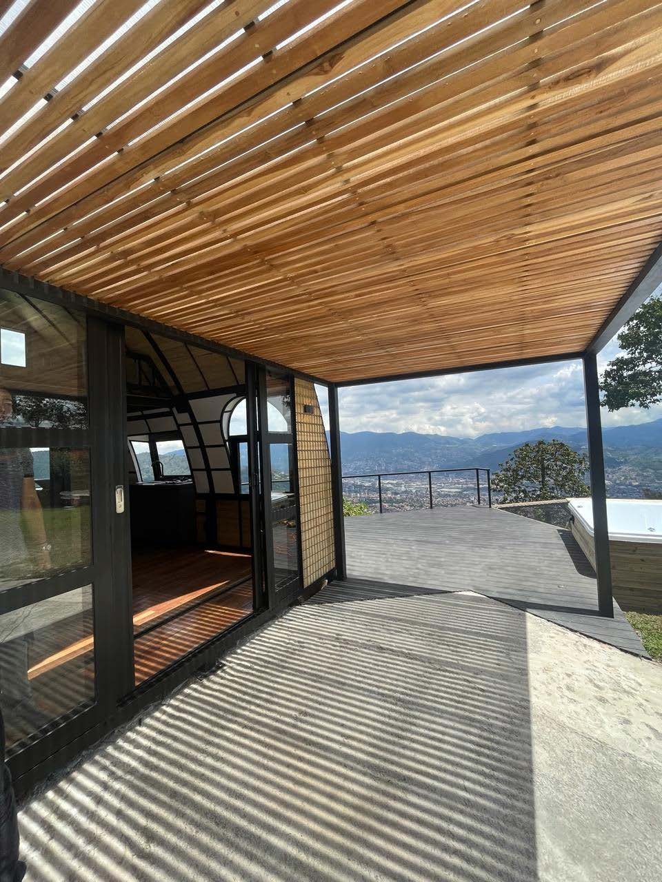 Terraza con techo de madera, ventanales de vidrio, jacuzzy y vista panorámica de montañas y ciudad.