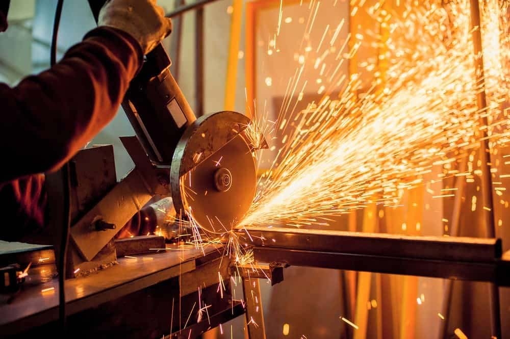 Persona usando una sierra eléctrica que genera chispas mientras corta metal en un taller.