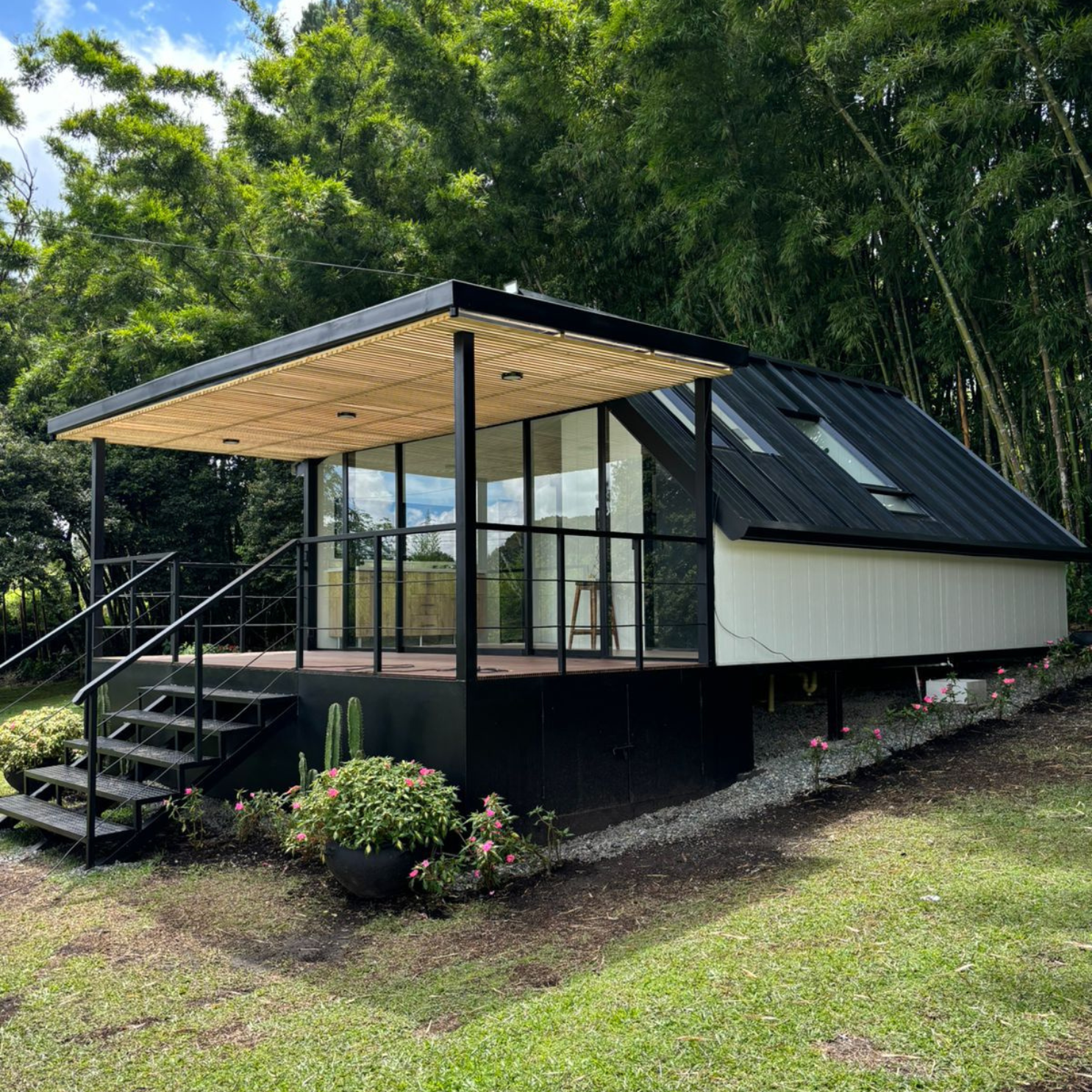 Casa moderna con paredes blancas y techo negro, con terraza de vidrio y jardín verde.