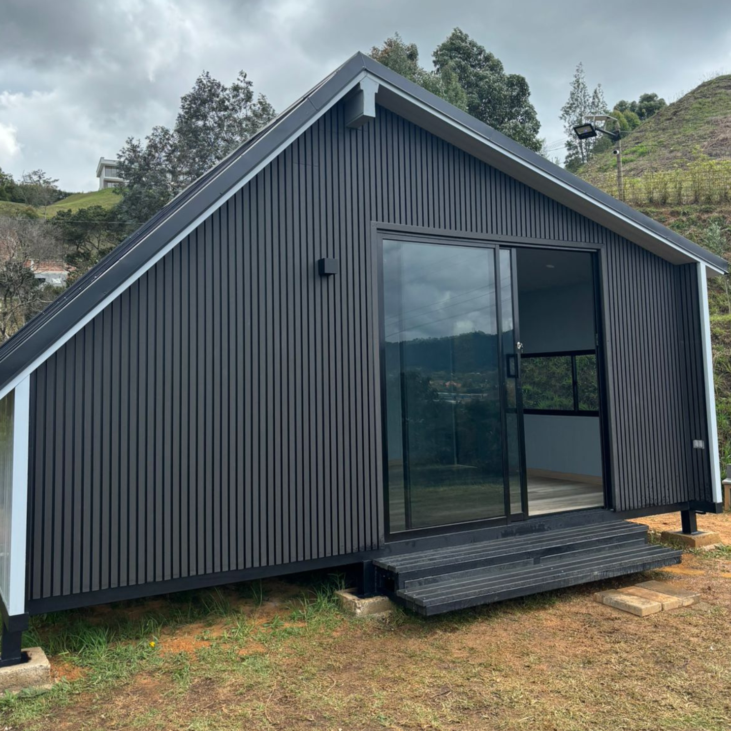 Casa negra moderna con paredes verticales y puerta corrediza de vidrio en entorno natural montañoso.